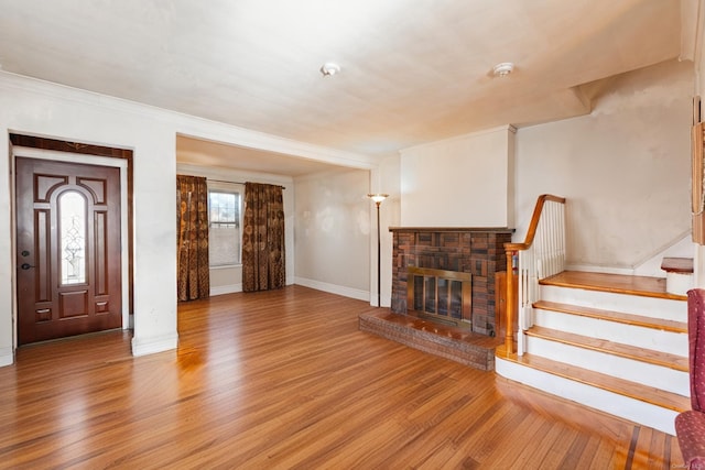 living room featuring wood-type flooring, a stone fireplace, and crown molding