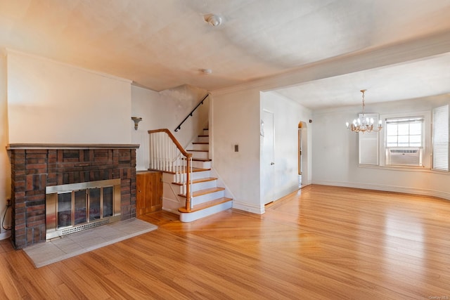 unfurnished living room featuring light wood-type flooring, cooling unit, crown molding, a fireplace, and a chandelier