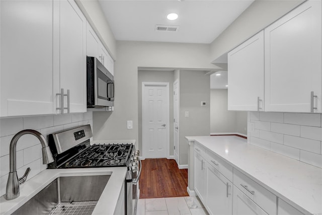 kitchen with white cabinets, appliances with stainless steel finishes, light stone countertops, and sink