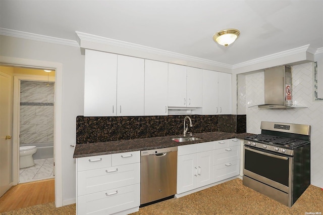 kitchen featuring sink, wall chimney range hood, appliances with stainless steel finishes, white cabinets, and ornamental molding