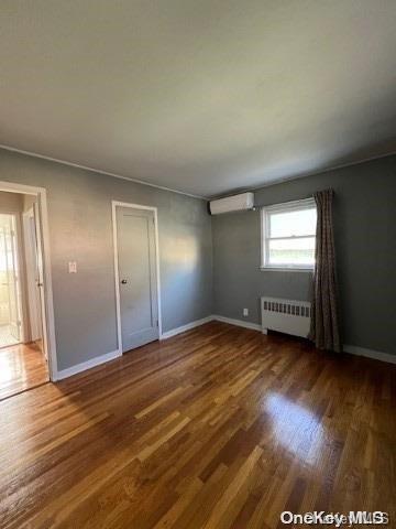 interior space with dark hardwood / wood-style floors, radiator heating unit, and a wall mounted AC