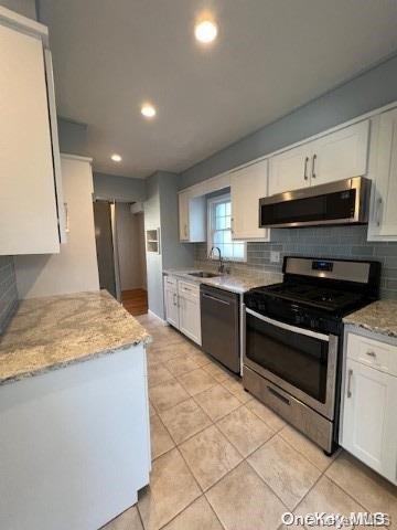 kitchen featuring white cabinets, light stone counters, appliances with stainless steel finishes, and tasteful backsplash