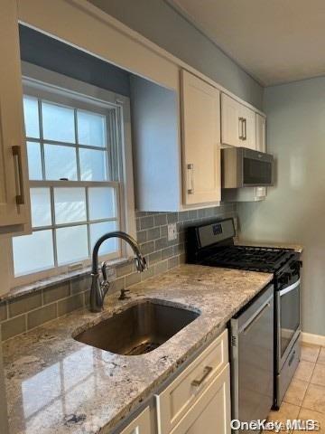 kitchen with sink, decorative backsplash, light stone counters, white cabinetry, and stainless steel appliances