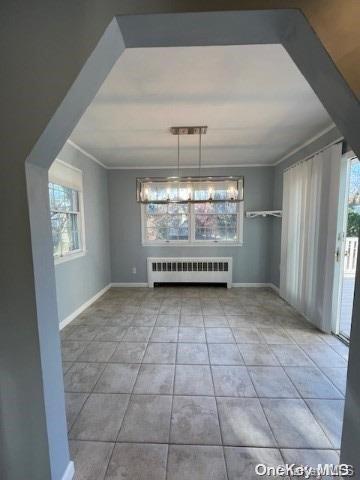 unfurnished dining area featuring light tile patterned floors, plenty of natural light, radiator, and crown molding