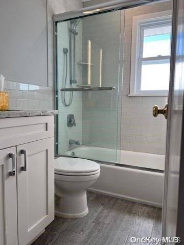 full bathroom with toilet, vanity, bath / shower combo with glass door, and hardwood / wood-style flooring