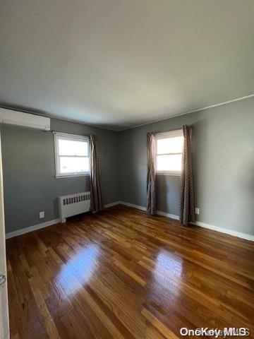 empty room with plenty of natural light, dark hardwood / wood-style flooring, and radiator heating unit