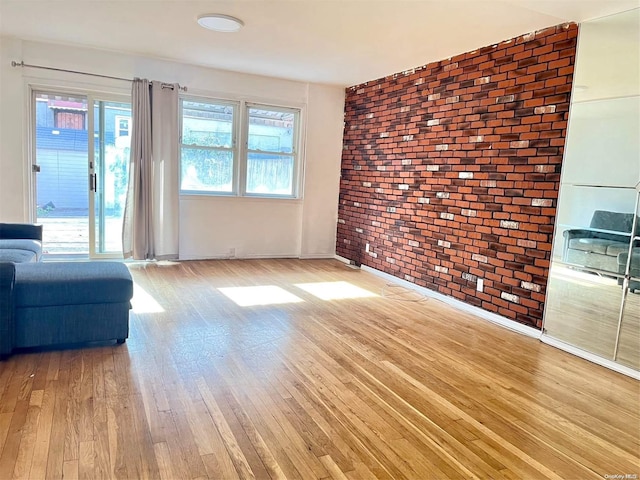 unfurnished living room featuring light hardwood / wood-style floors, a healthy amount of sunlight, and brick wall