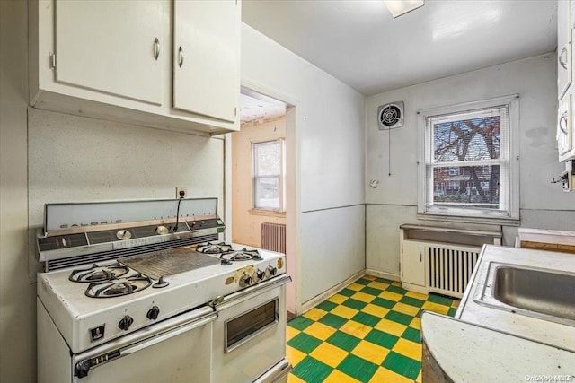 kitchen with white cabinets, stainless steel gas range oven, and radiator heating unit