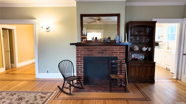 living room featuring ceiling fan, sink, a brick fireplace, hardwood / wood-style flooring, and ornamental molding