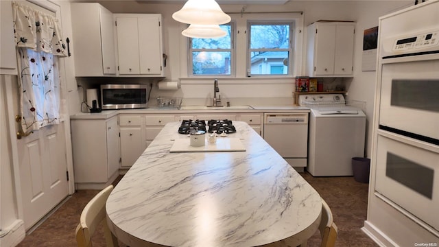 kitchen with hanging light fixtures, sink, appliances with stainless steel finishes, white cabinetry, and washer / clothes dryer