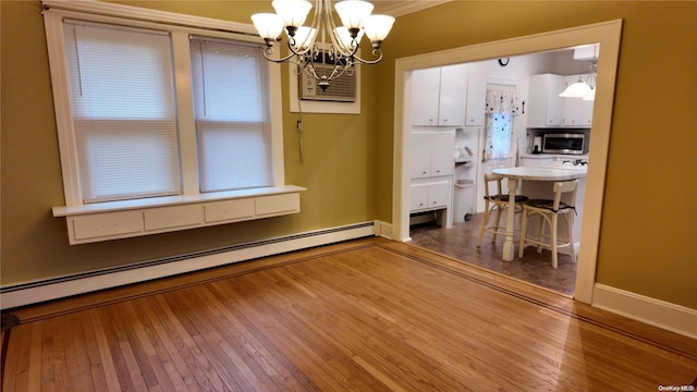 unfurnished dining area with a chandelier, wood-type flooring, a baseboard radiator, and crown molding