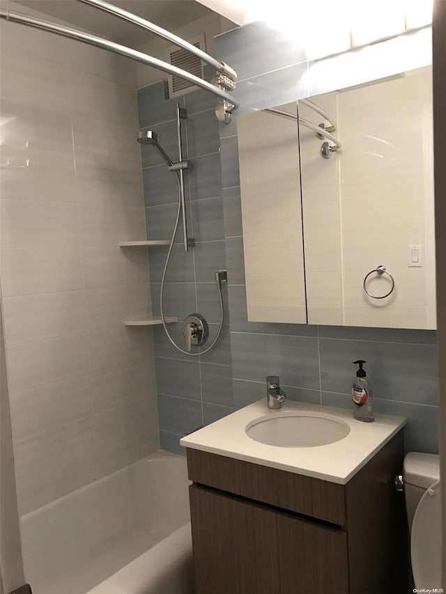 full bathroom with backsplash, vanity, tile walls, toilet, and tiled shower / bath