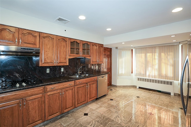 kitchen with sink, radiator heating unit, tasteful backsplash, dark stone countertops, and appliances with stainless steel finishes