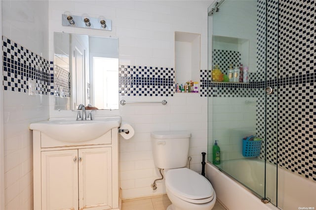 full bathroom with combined bath / shower with glass door, vanity, tile walls, tile patterned flooring, and toilet