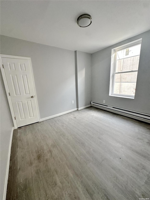 empty room with wood-type flooring and a baseboard heating unit