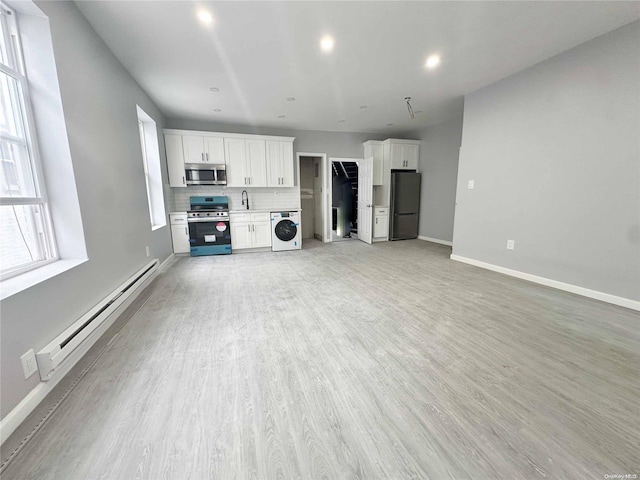 unfurnished living room featuring washer / dryer, light wood-type flooring, a baseboard radiator, and sink