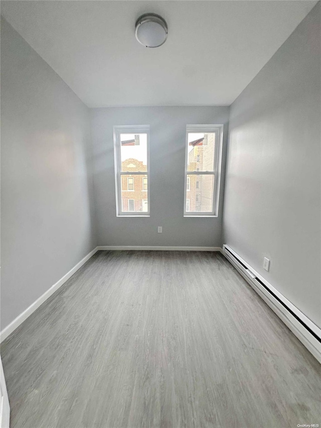 unfurnished room with a baseboard heating unit and hardwood / wood-style flooring