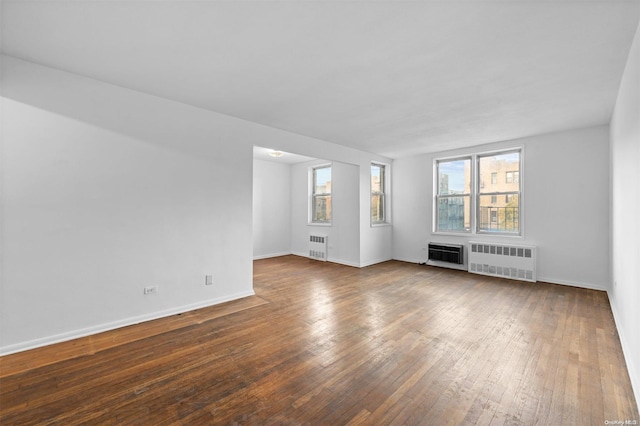 unfurnished living room with dark hardwood / wood-style flooring, a wall unit AC, and radiator