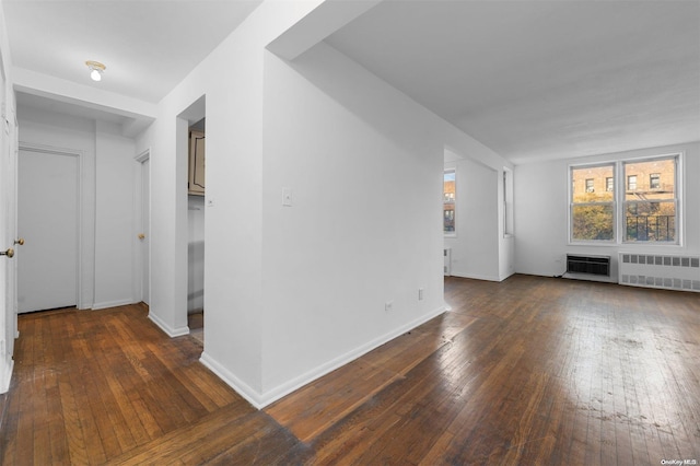 unfurnished living room featuring a wall mounted air conditioner, dark hardwood / wood-style floors, and radiator