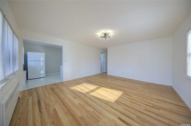 unfurnished room with light hardwood / wood-style floors, radiator heating unit, and an inviting chandelier