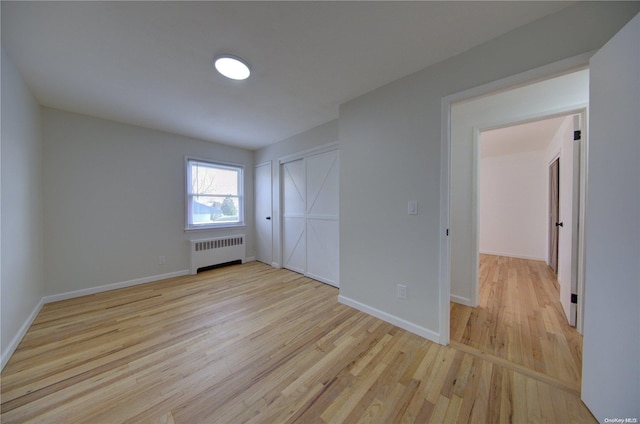 unfurnished bedroom featuring radiator heating unit and light hardwood / wood-style floors