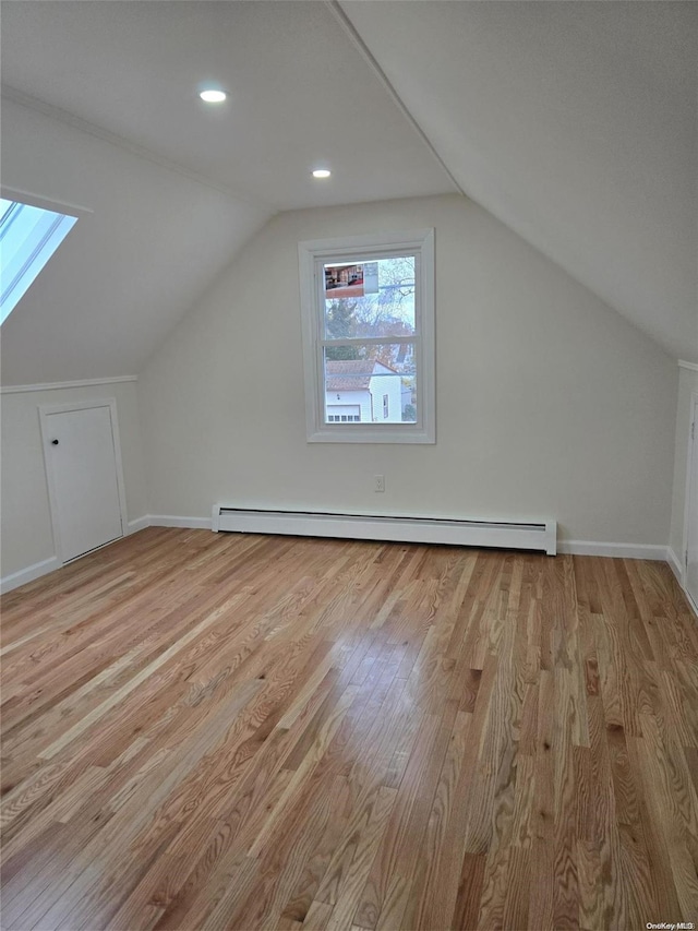 additional living space featuring baseboard heating, vaulted ceiling, and light wood-type flooring