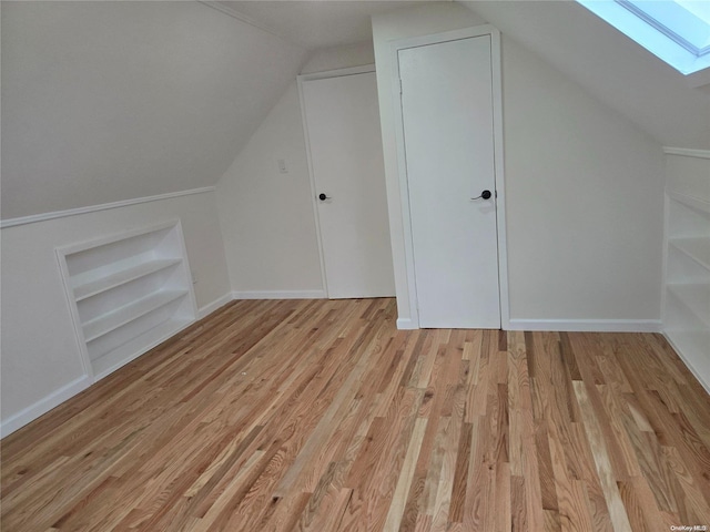 additional living space with built in shelves, vaulted ceiling with skylight, and light hardwood / wood-style flooring