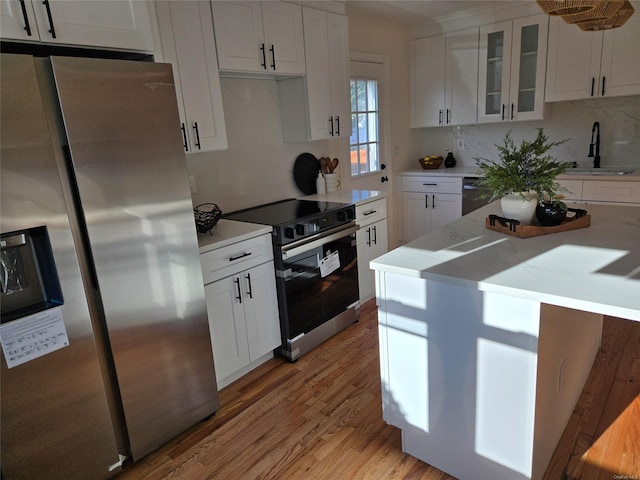 kitchen featuring sink, backsplash, appliances with stainless steel finishes, white cabinets, and light wood-type flooring