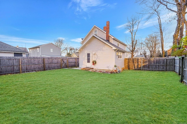 rear view of house with a yard, a chimney, and a fenced backyard