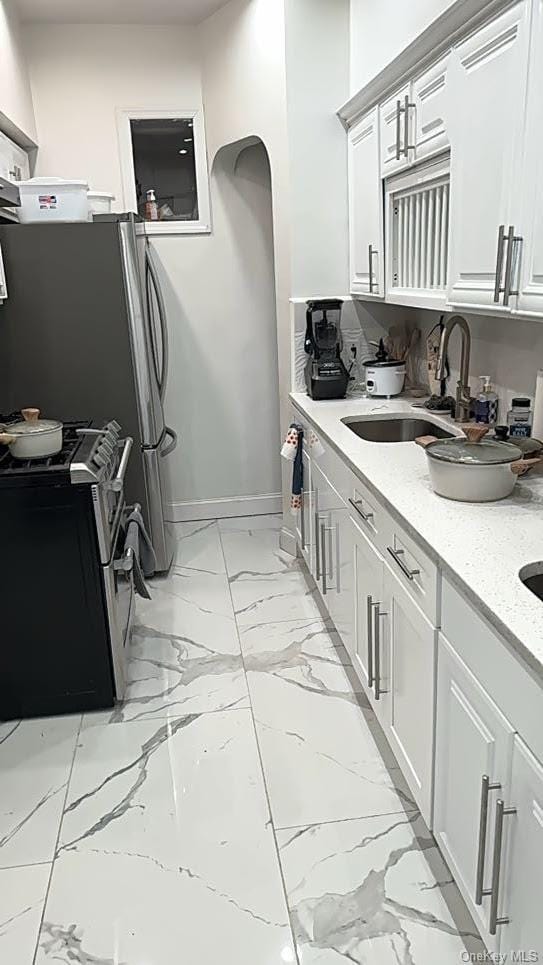 kitchen featuring white cabinetry, sink, light stone counters, and range with two ovens