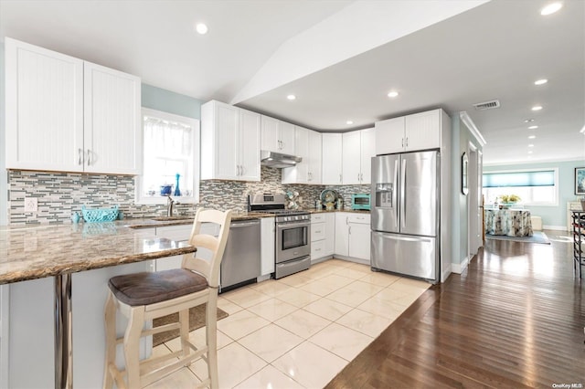 kitchen with kitchen peninsula, appliances with stainless steel finishes, tasteful backsplash, light stone counters, and white cabinetry