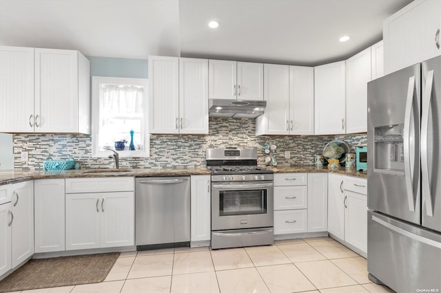 kitchen featuring appliances with stainless steel finishes, tasteful backsplash, sink, dark stone countertops, and white cabinetry