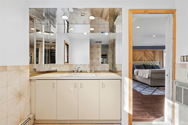 bathroom featuring hardwood / wood-style flooring, vanity, baseboard heating, and tasteful backsplash