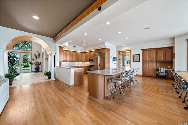 kitchen with stainless steel appliances, light stone counters, light hardwood / wood-style floors, a kitchen bar, and a center island with sink