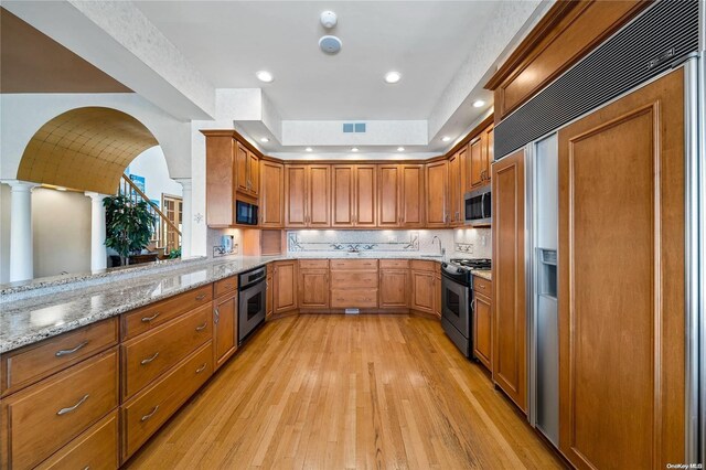 kitchen featuring light hardwood / wood-style flooring, built in appliances, light stone counters, kitchen peninsula, and decorative columns