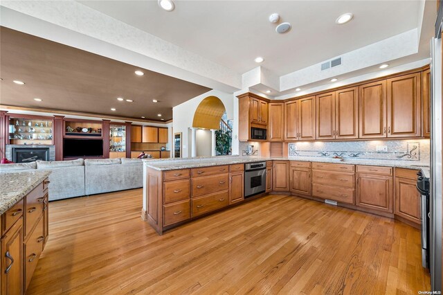 kitchen featuring light stone countertops, stainless steel appliances, light hardwood / wood-style flooring, backsplash, and kitchen peninsula