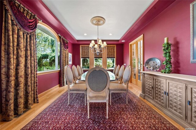 dining area with french doors, light hardwood / wood-style floors, a raised ceiling, and a notable chandelier