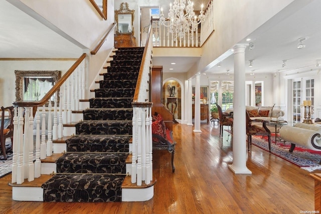 foyer entrance with a high ceiling, a notable chandelier, decorative columns, crown molding, and hardwood / wood-style floors