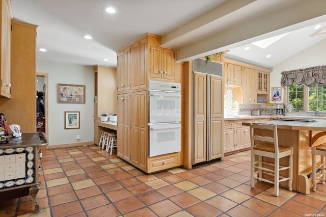 kitchen with white double oven, light brown cabinets, paneled fridge, decorative backsplash, and a breakfast bar