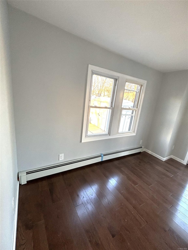 spare room featuring baseboard heating and dark hardwood / wood-style floors