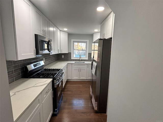 kitchen featuring appliances with stainless steel finishes, light stone countertops, sink, white cabinetry, and tasteful backsplash