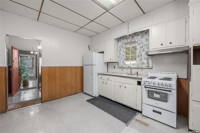 kitchen featuring white cabinetry, a drop ceiling, sink, wood walls, and white appliances