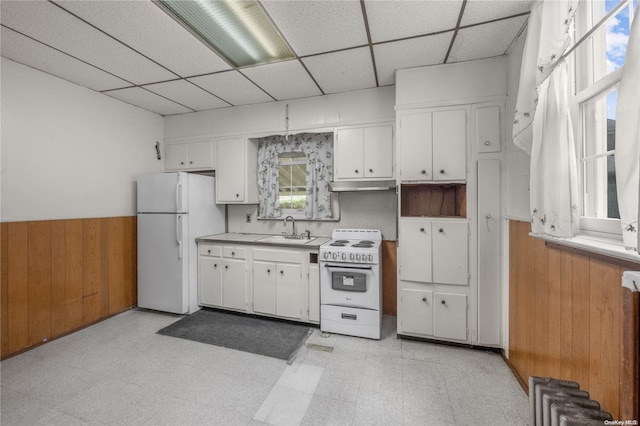 kitchen featuring white appliances, white cabinetry, a paneled ceiling, and wood walls