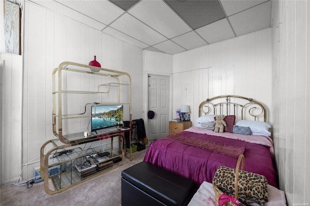 bedroom with wood walls, a drop ceiling, and carpet