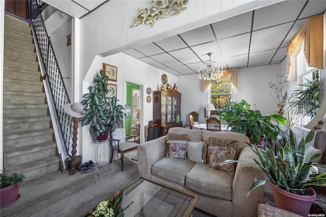 living room featuring a wealth of natural light, a drop ceiling, a chandelier, and wood walls