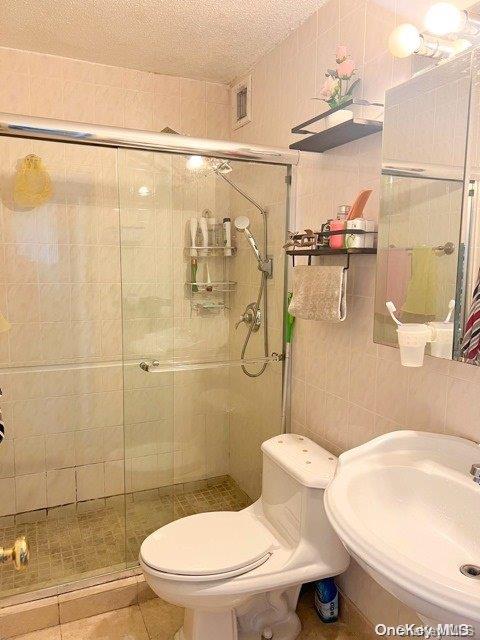 bathroom featuring tile patterned floors, a textured ceiling, sink, tile walls, and toilet