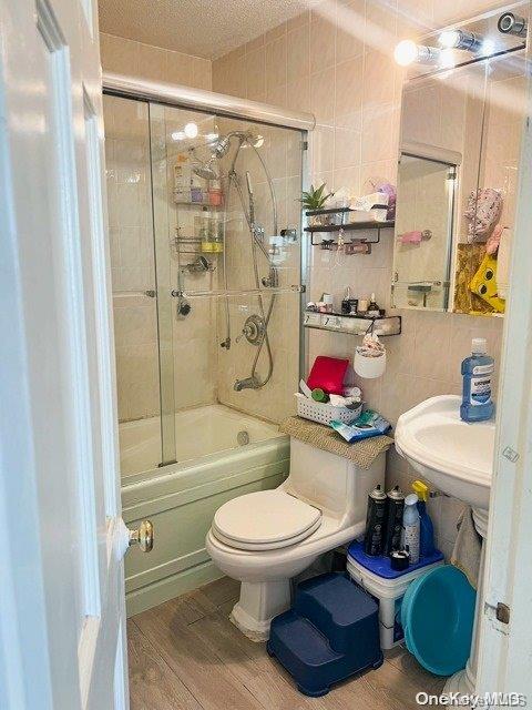 bathroom with hardwood / wood-style floors, combined bath / shower with glass door, toilet, a textured ceiling, and tile walls