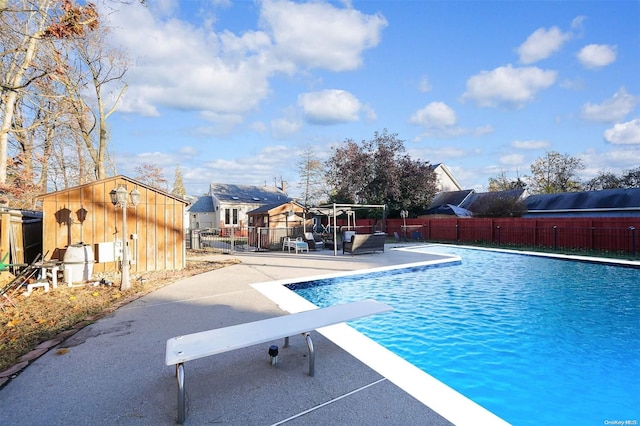 view of swimming pool featuring a patio, a diving board, and a storage shed