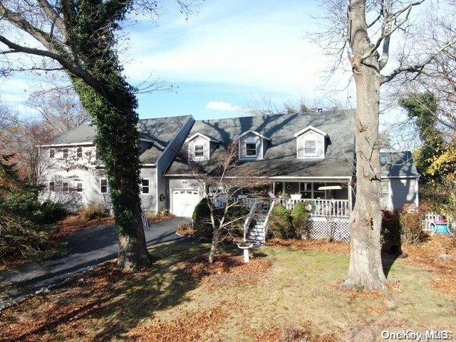 new england style home with a garage, a front lawn, and covered porch