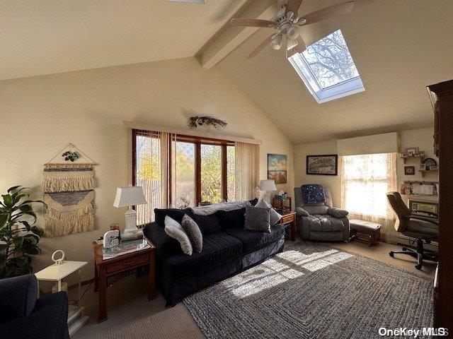 living room with ceiling fan, a skylight, high vaulted ceiling, carpet flooring, and beamed ceiling